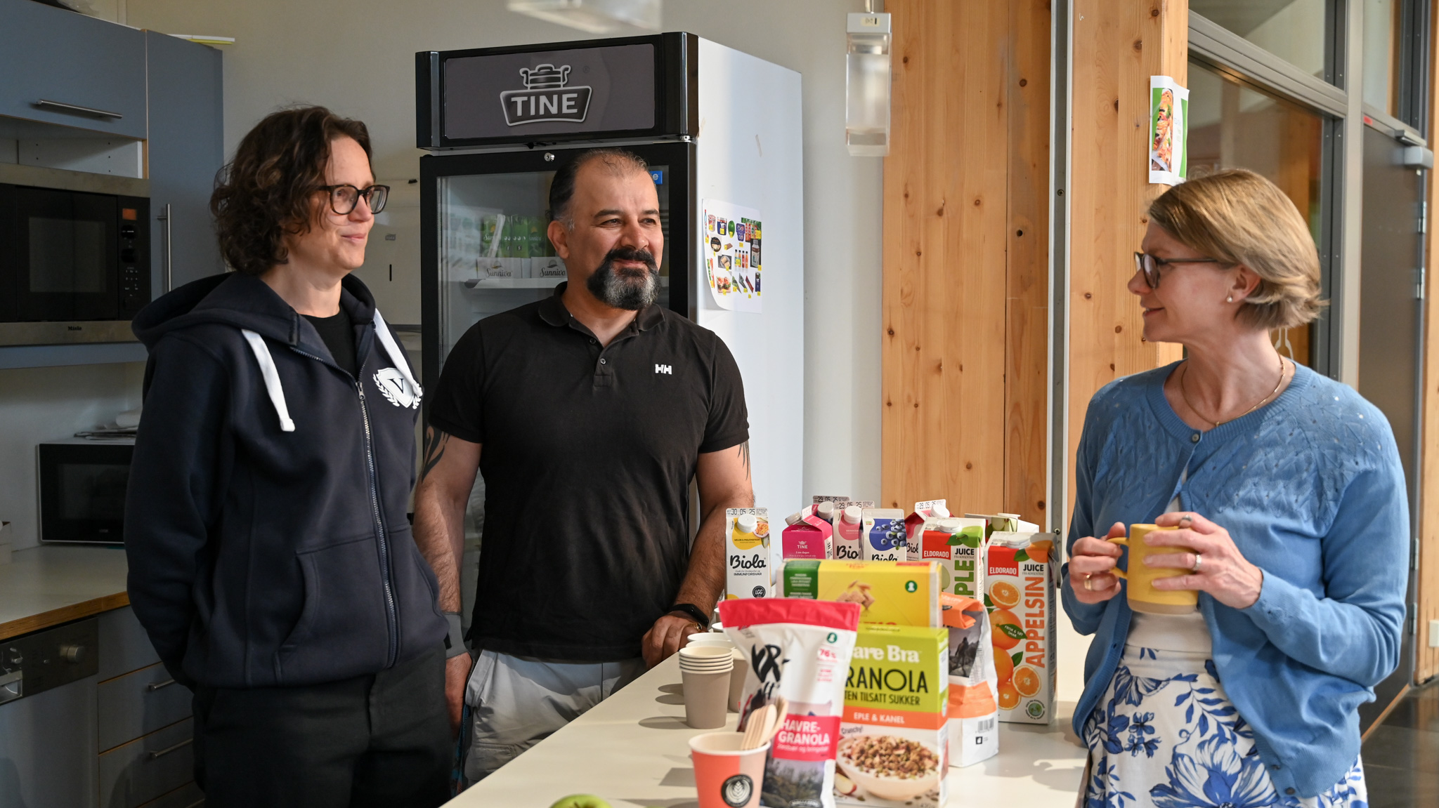 Miljøterapeut Nina Haukeland, miljøarbeider Rashad Tayeri og rektor Hanne Vislie står sammen i et kjøkkenområde med mat- og drikkevarer rundt seg.